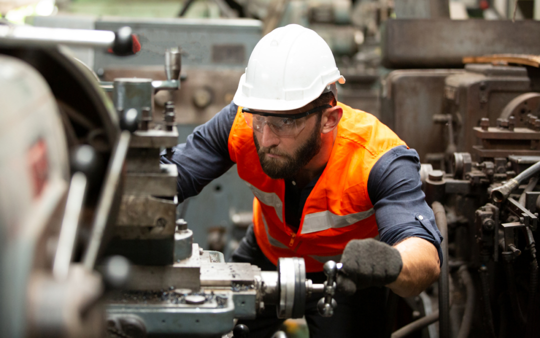Man working on machine with safety hat, vest, glasses, and gloves on.